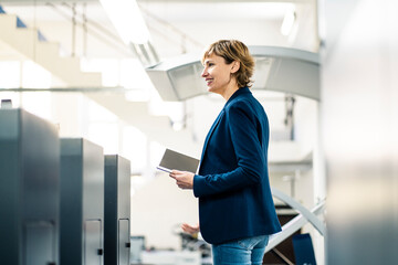 Smiling female manager with digital tablet standing at printing factory