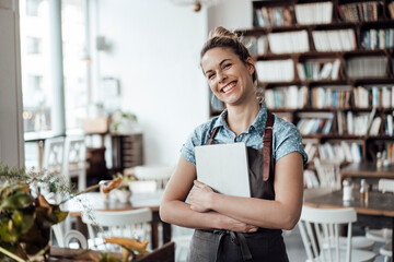 Cheerful mid adult waitress holding digital tablet at cafe