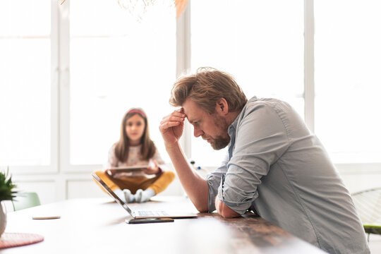 Worried businessman looking at laptop with girl in background on table