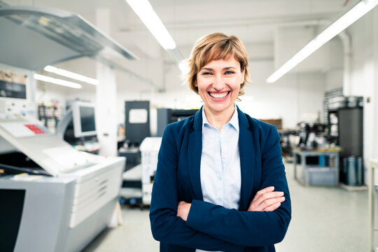 Cheerful businesswoman with arms crossed in printing factory
