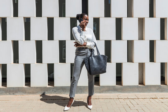 Mid adult businesswoman with purse talking on mobile phone during sunny day