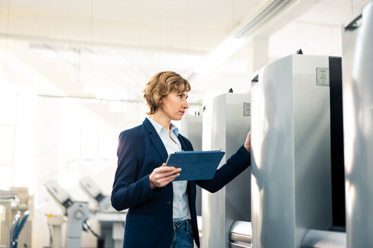 Female manager with digital tablet checking machine while standing in factory
