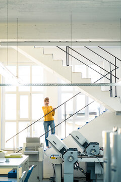 Mature owner talking on mobile phone while standing in printing industry
