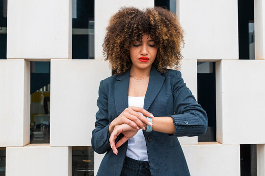 Attractive businesswoman wearing wristwatch checking time in front of modern wall