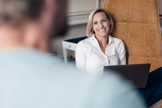 Smiling woman with laptop looking at man at home