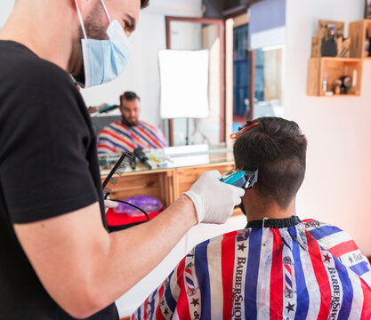 Male hairstylist cutting hair of customer with machine at barber shop
