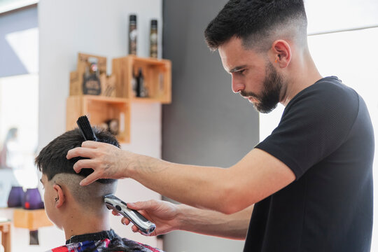 Male barber using machine to cut hair of teenage boy at salon