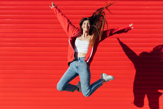 Teenage girl with tousled hair jumping in front of red wall