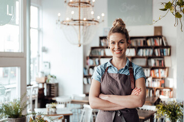 Confident mid adult waitress standing with arms crossed at coffee shop
