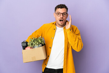 Young caucasian man making a move while picking up a box full of things isolated on purple...
