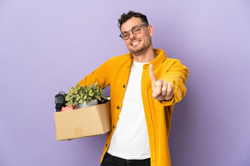 Young caucasian man making a move while picking up a box full of things isolated on purple...
