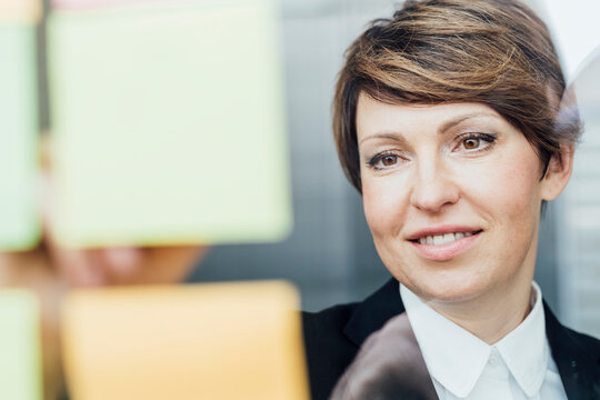 Contented businesswoman looking at adhesive notes sticked on glass wall in office