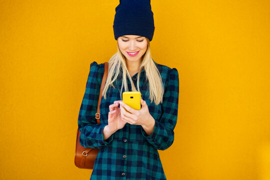 Smiling woman in knit hat using mobile phone in front of wall