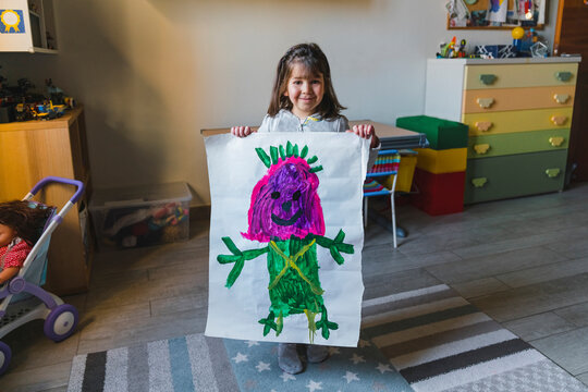 Smiling girl holding drawing at home