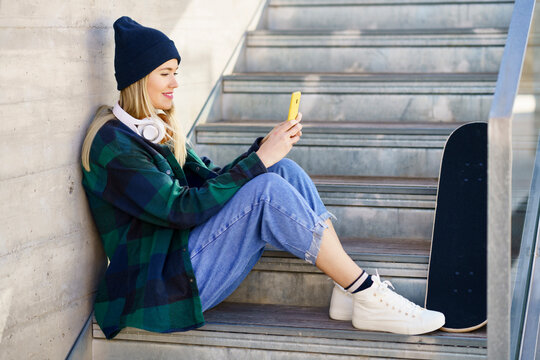 Smiling woman in knit hat using mobile phone on steps