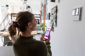 Young woman using smart home function on mobile phone at home