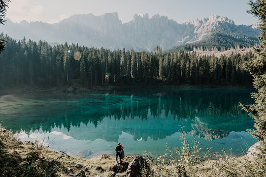 Man and woman standing on rock at Carezza lake during sunny day in South Tyrol, Italy