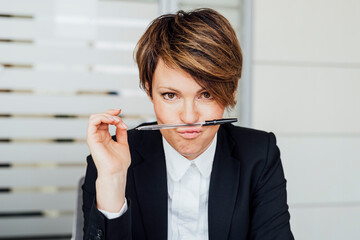 Playful female entrepreneur balancing pen on lips in while sitting in office