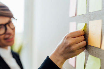 Businesswoman sticking adhesive note on wall in office