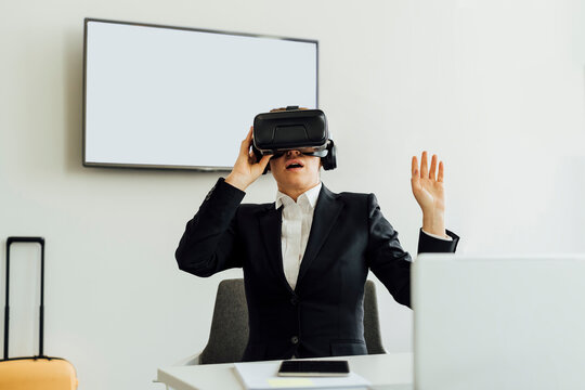 Mature female professional watching virtual reality simulator while sitting at desk in office