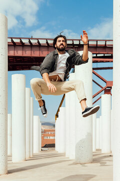 Excited young man jumping between columns on sunny day