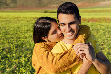 Girlfriend embracing boyfriend while standing at meadow during sunny day