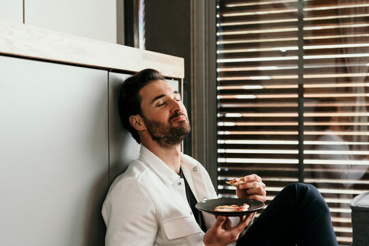 Handsome man eating while sitting near window at home