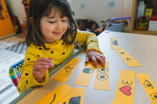 Cute girl playing with smileys on table in playroom at home