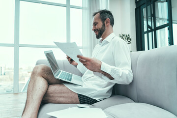 Businessman with laptop holding document while sitting on sofa at home