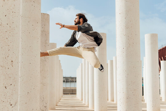 Carefree young man jumping between white columns on sunny day
