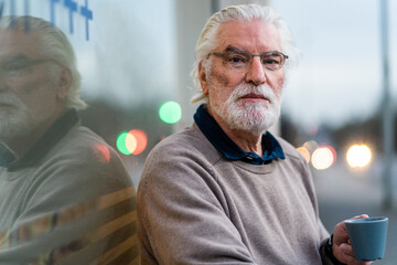 Handsome man with gray hair holding coffee cup sitting outside cafe