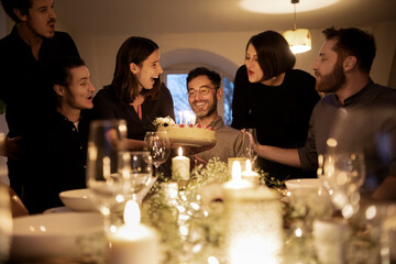Male and female friends cheering during birthday celebration of smiling man at home