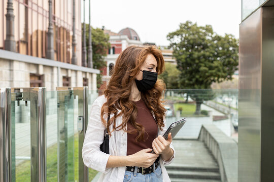 Young woman wearing protective face mask standing with digital tablet