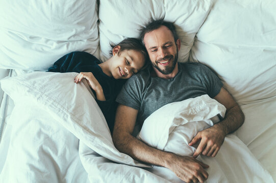 Father and son with blanket lying on bed at home