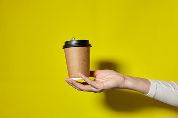 Hands holding two cups brown paper with black lid. Two coffee special offer or promo. Hands holding two cups on yellow screen background. Tea or Coffee to go. Brown paper cup with black lid.