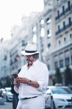 Senior man with white clothing and hat using smart phone in street of Madrid