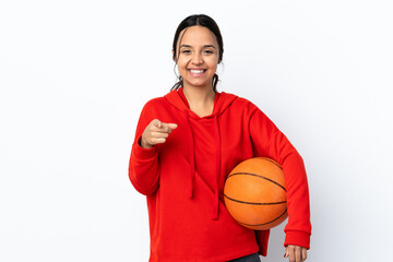 Young woman playing basketball over isolated white background surprised and pointing front