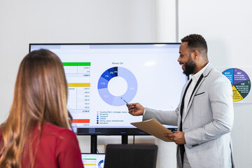 Male entrepreneur explaining data over television to colleague in meeting