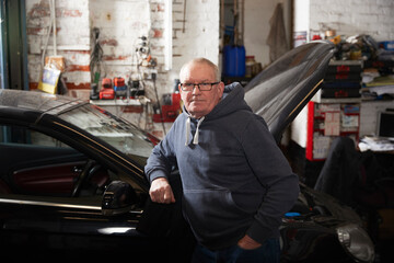 Confident male mechanic with hand in pocket leaning on car at workshop