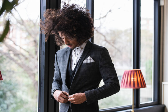 Young businessman buttoning suit while standing in cafe