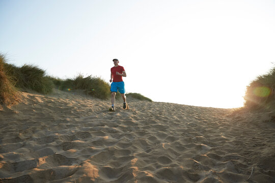 Male athlete running on sand dune at sunrise
