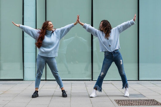 Friends wearing blue sweater giving high-five while standing on footpath