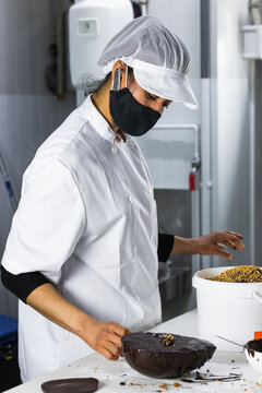 Female baker with face mask preparing chocolate dessert in kitchen