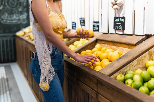 Woman with mesh bag buying lemons at supermarket