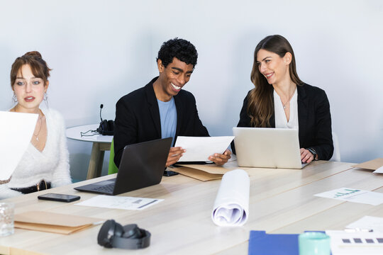Young business people smiling while sitting by colleagues in meeting