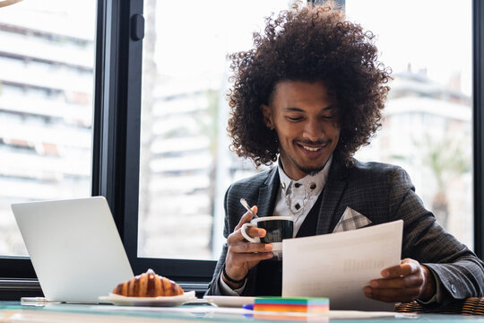 Smiling male freelancer examining document while having coffee in cafe