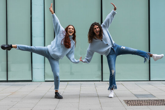 Carefree friends standing on one leg in front of wall