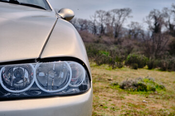 Front head light of the a italian designed car in nature with tree and forrest background.
