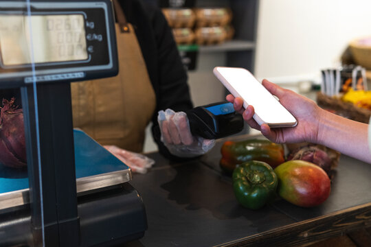 Woman holding smart phone over credit card reader while paying at grocery store