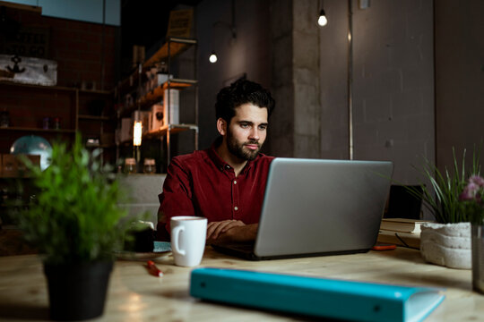 Mid adult male freelancer with coffee cup working on laptop in cafe